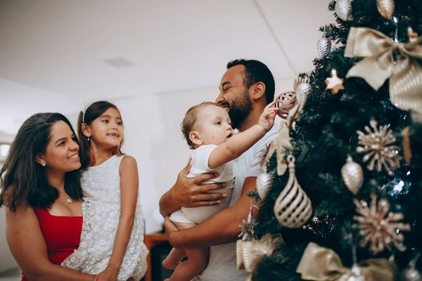 Family hanging ornaments on a decorated Christmas tree in a bright living room