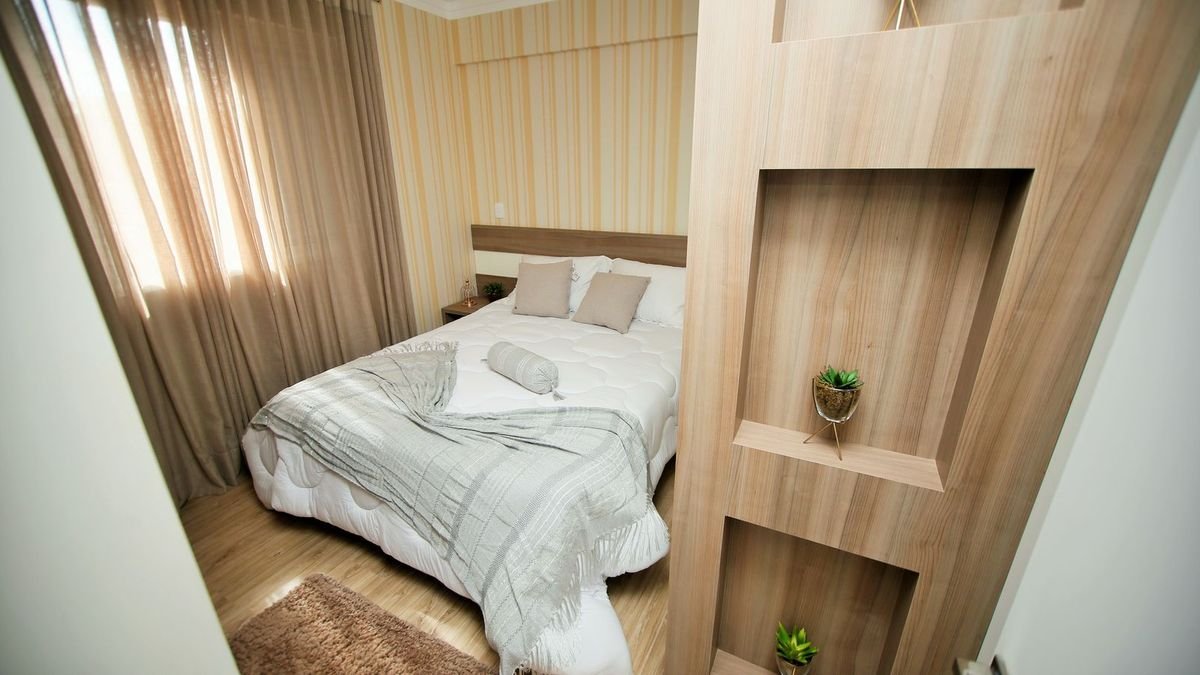 Modern bedroom with a soft gray blanket over a white bed, warm wood paneling, and sheer curtains