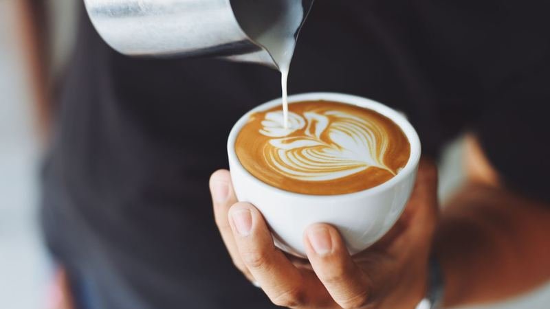 Hands pouring steamed milk for latte art over espresso
