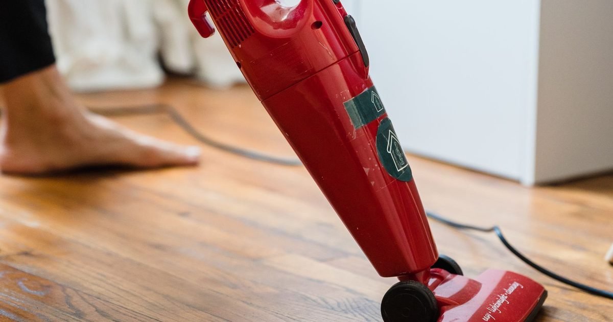 Person cleaning a wood floor with a red stick vacuum