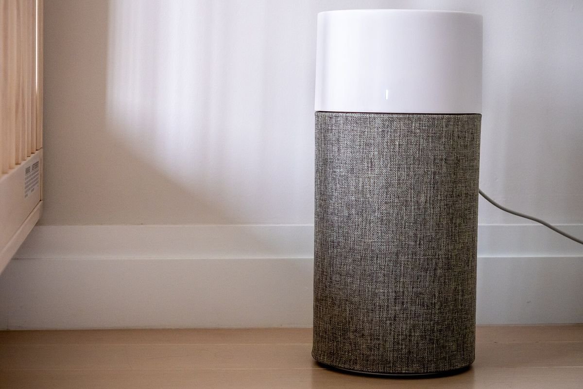 Cylindrical air purifier with a gray fabric pre-filter by a window (representative photo, not the exact product)