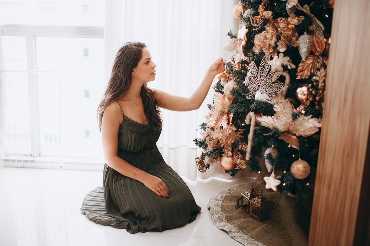 Woman kneeling to hang ornaments on a Christmas tree in a bright white room