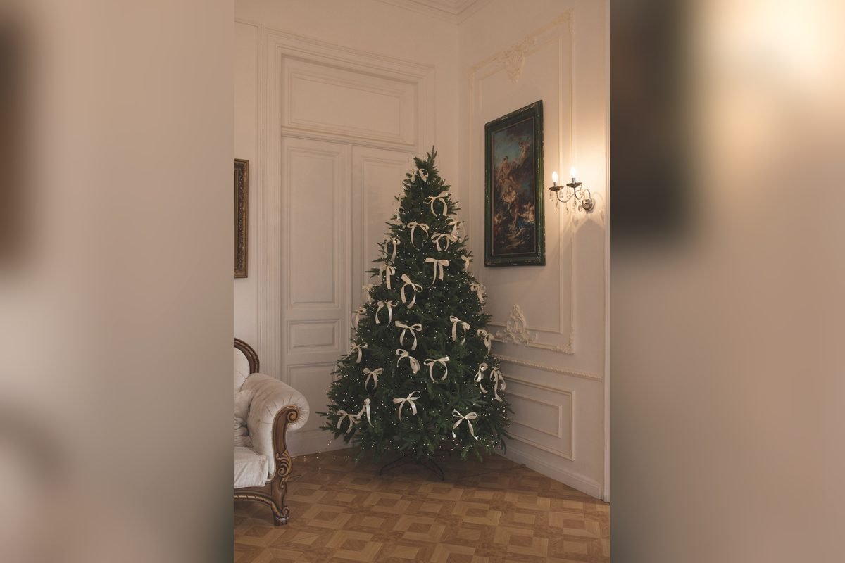 Dense green Christmas tree with white bows in a classic white-paneled room (representative photo, not the exact product)