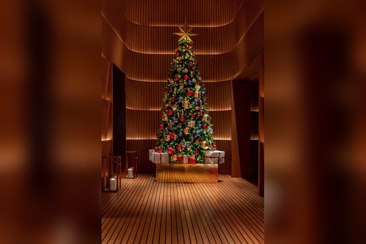Tall, narrow Christmas tree with multicolor ornaments and a gold star in a wood-paneled room (representative photo, not the exact product)