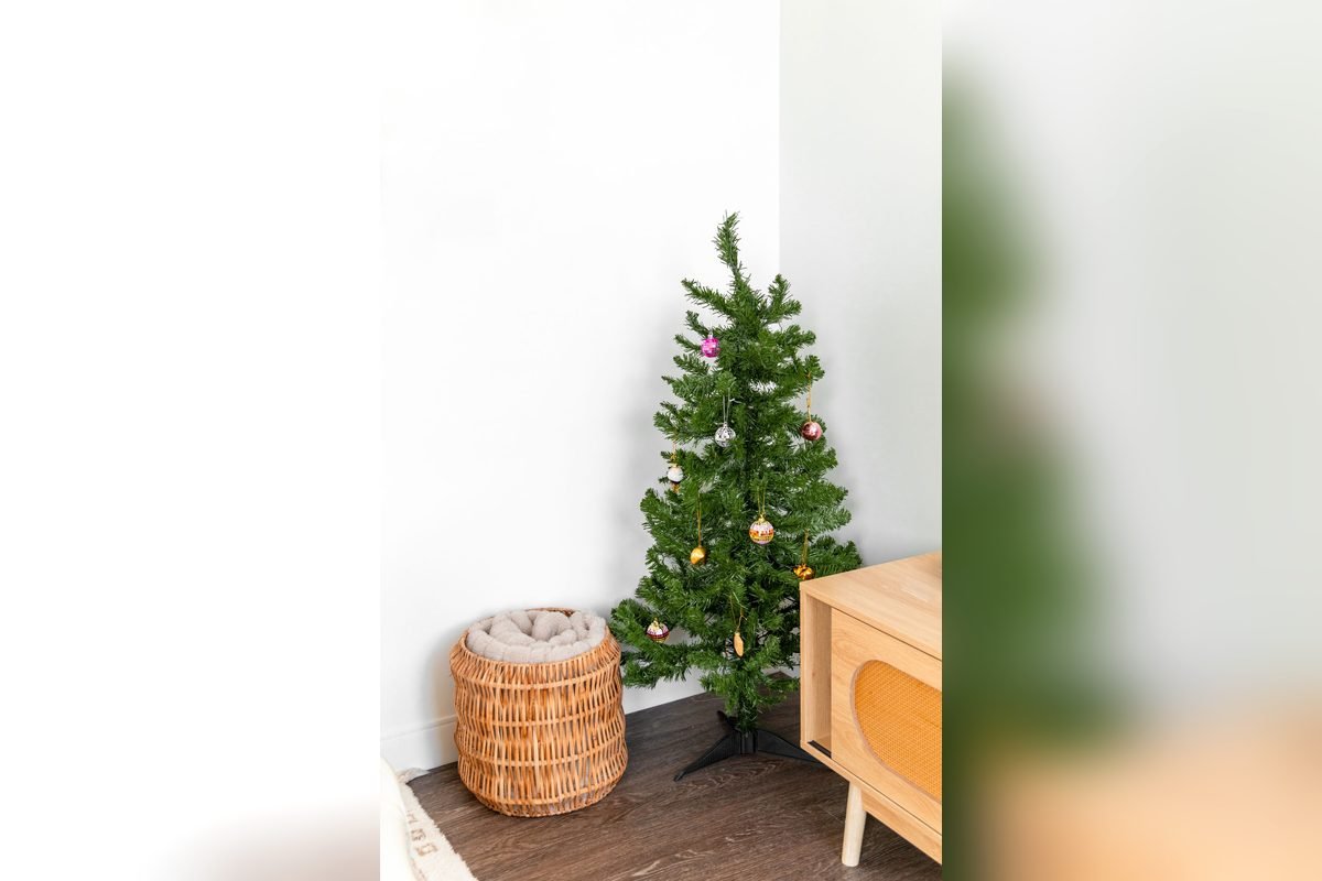 Simple small green Christmas tree on a metal stand next to a woven basket in a white room (representative photo, not the exact product)