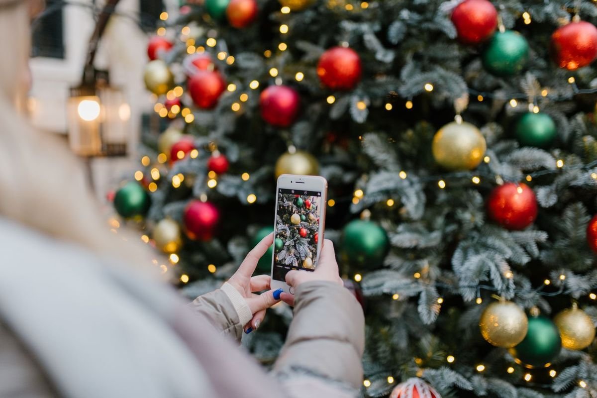 Person taking a smartphone photo of a lit Christmas tree with red and gold ornaments (representative photo, not the exact product)