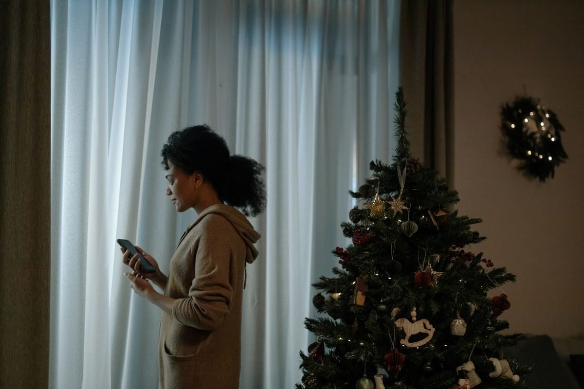 Woman holding a smartphone next to a decorated Christmas tree by a window (representative photo, not the exact product)