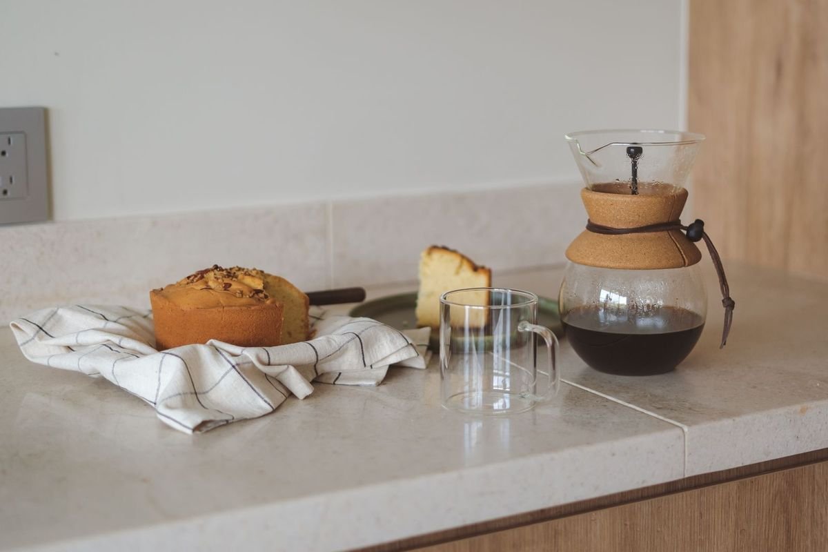 Glass coffee carafe, mugs and a loaf cake on a bright kitchen counter