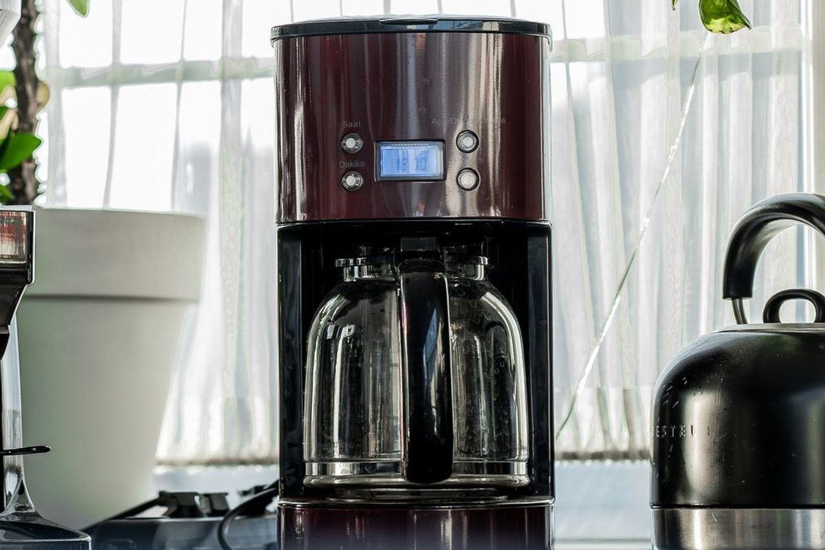 Burgundy and black programmable drip coffee maker with a glass carafe by a sunny kitchen window (representative photo, not the exact product)