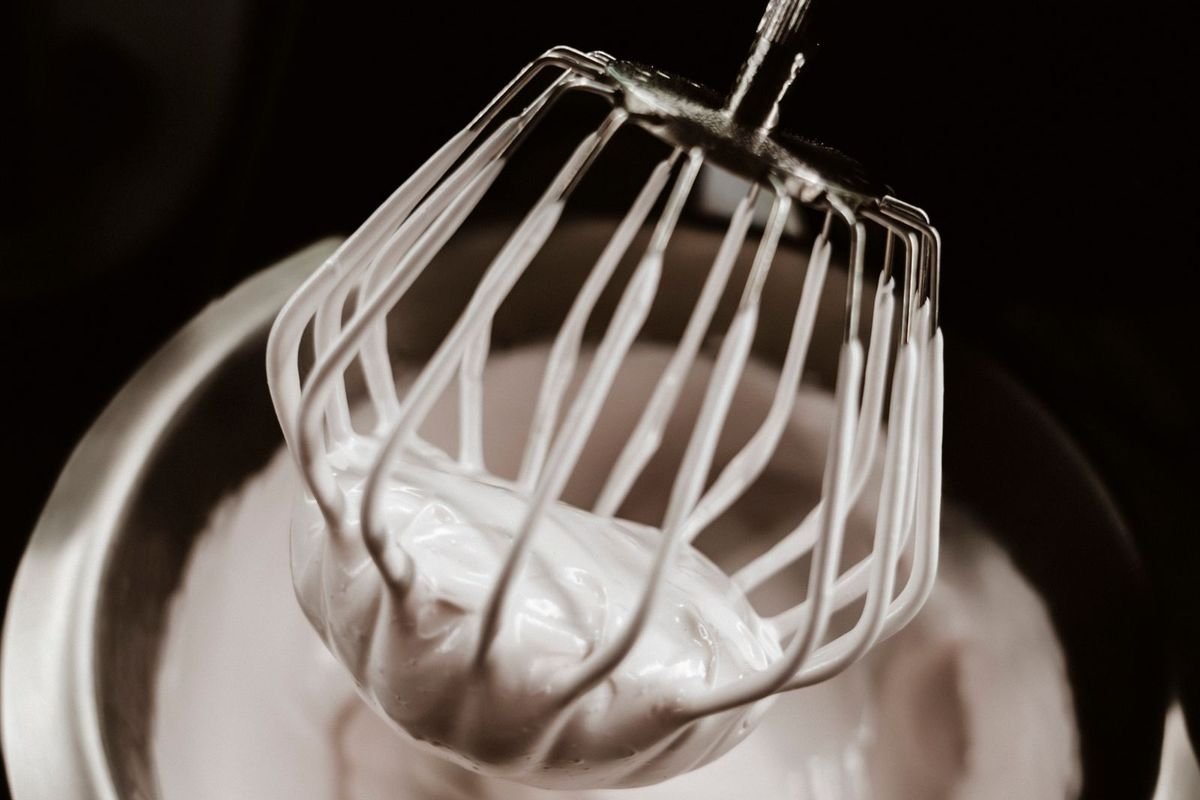 Stand mixer wire whisk lifted from a metal bowl of stiff whipped egg whites