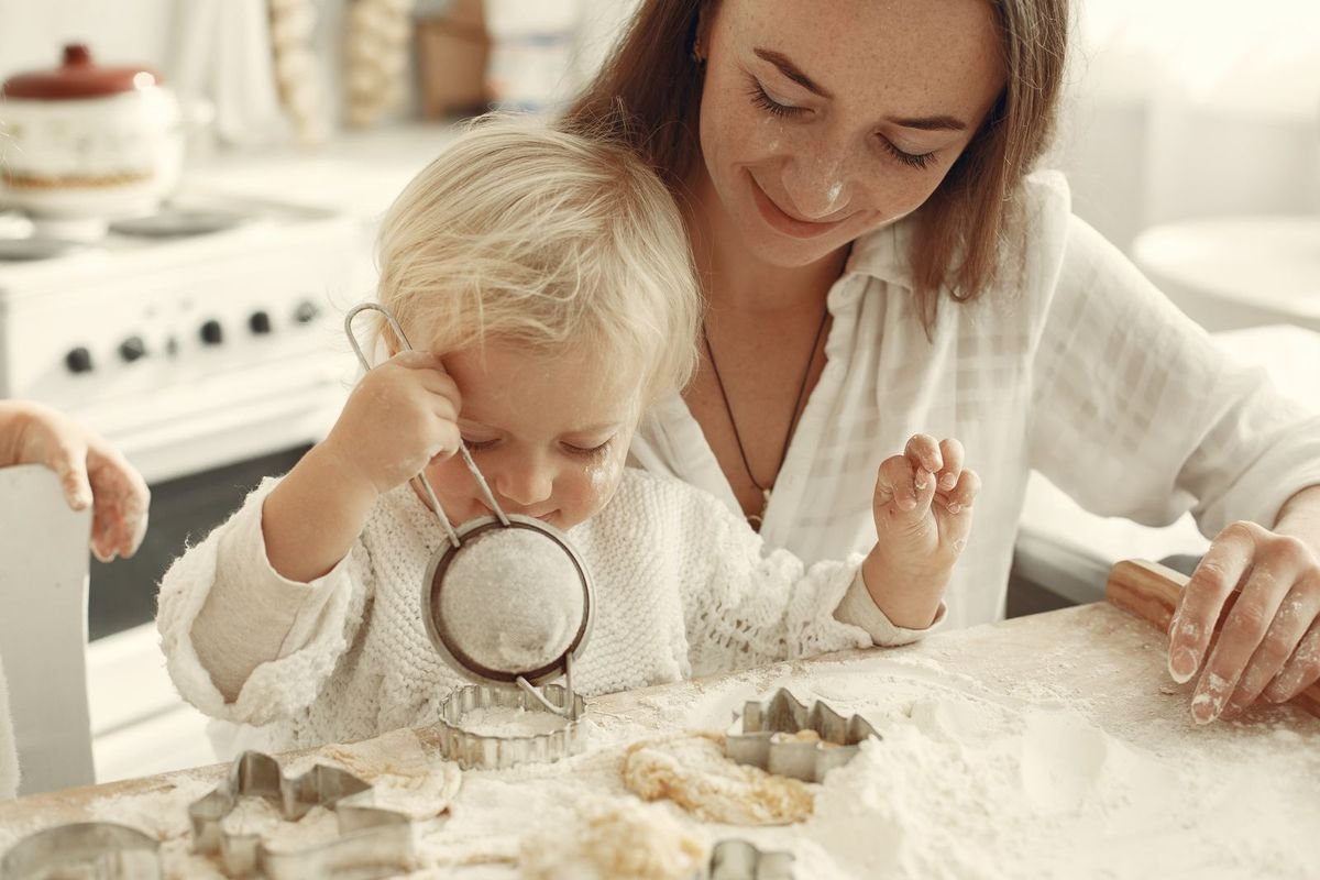 Mother and toddler cutting out cookies on a floured table in a bright kitchen