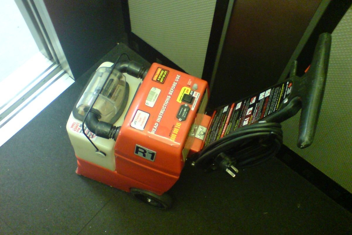 Red upright carpet cleaning machine on a dark carpet (representative photo, not the exact product)