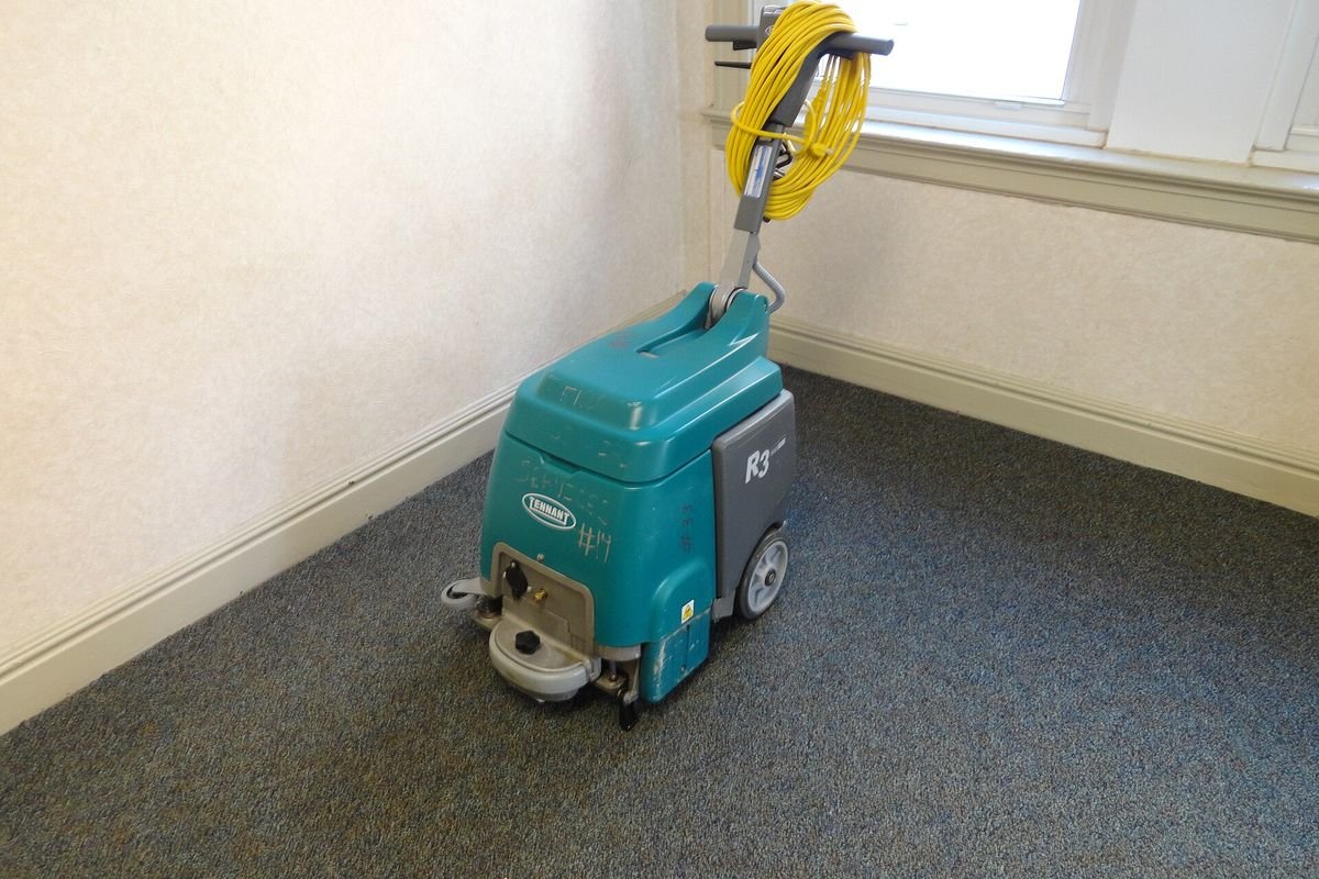 Teal commercial carpet extractor in an empty carpeted room (representative photo, not the exact product)