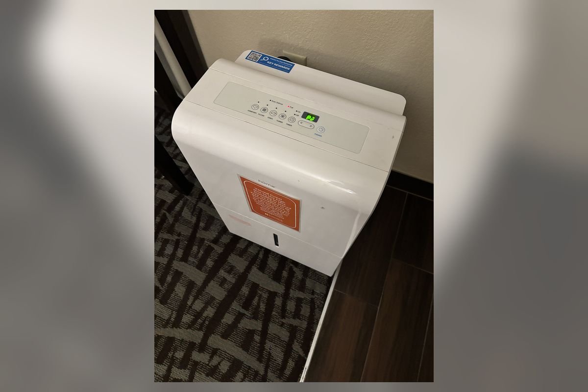 White portable dehumidifier on the floor of a hotel bedroom (representative photo, not the exact product)