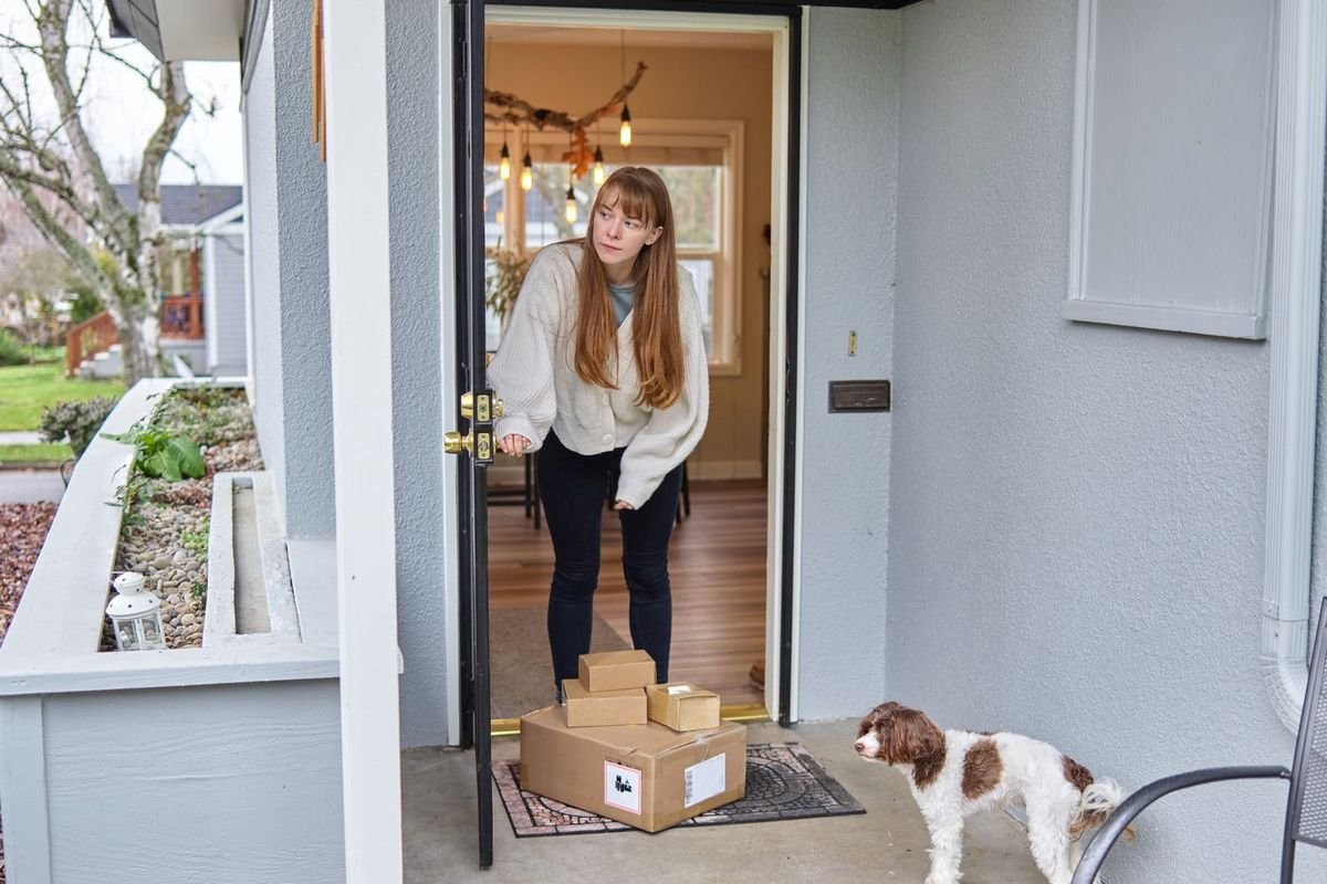 Woman opening her front door to collect packages while her dog watches