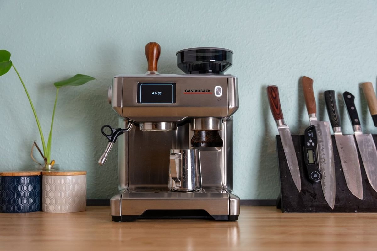 Stainless espresso machine with a bean hopper on a wooden kitchen counter with plants (representative photo, not the exact product)