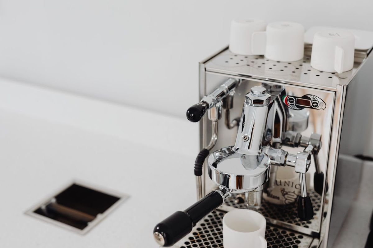 Polished stainless espresso machine with cups on top on a white counter (representative photo, not the exact product)