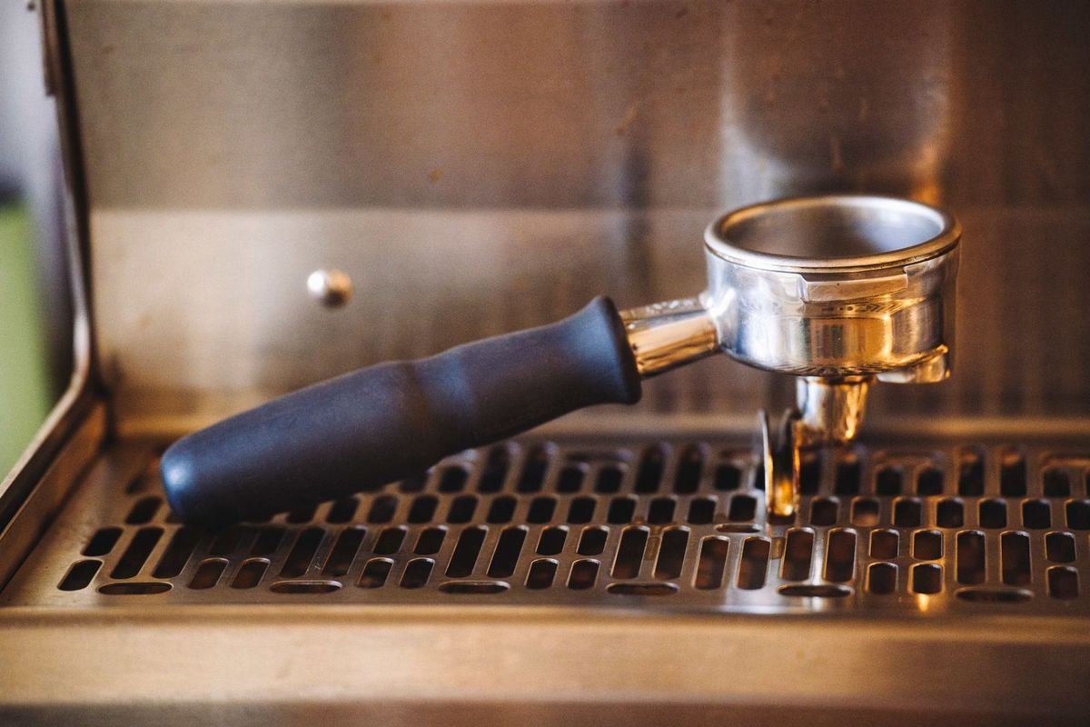 Close-up of a portafilter resting on a stainless espresso machine drip tray (representative photo, not the exact product)