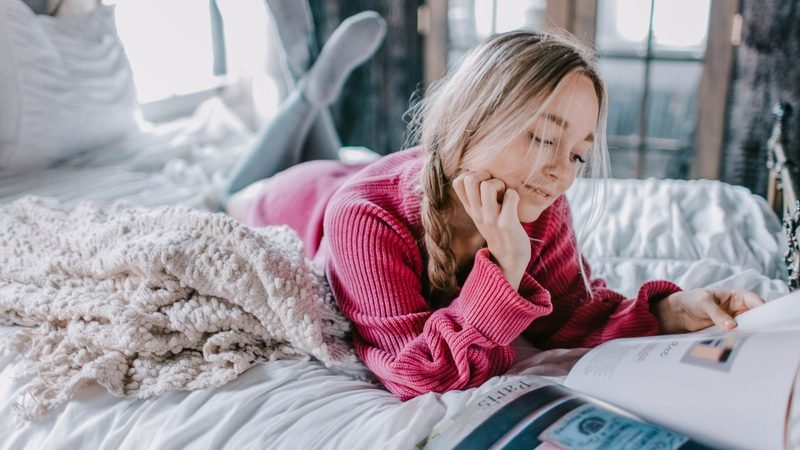 Woman in a cozy sweater relaxing on a bed with a magazine