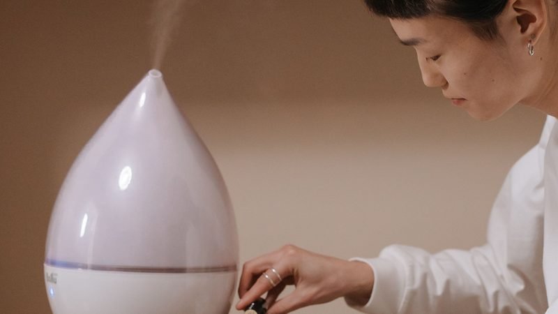 Person adjusting a white cool-mist humidifier releasing a soft plume of mist
