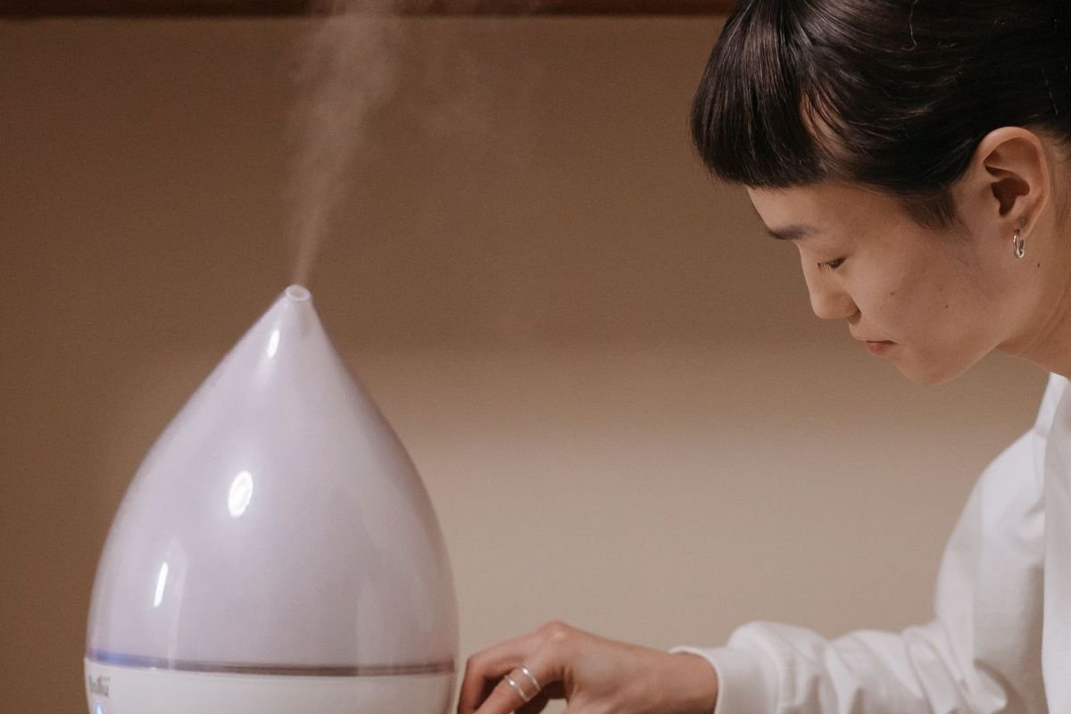 Person adjusting a compact white humidifier on a shelf in a minimalist room (representative photo, not the exact product)