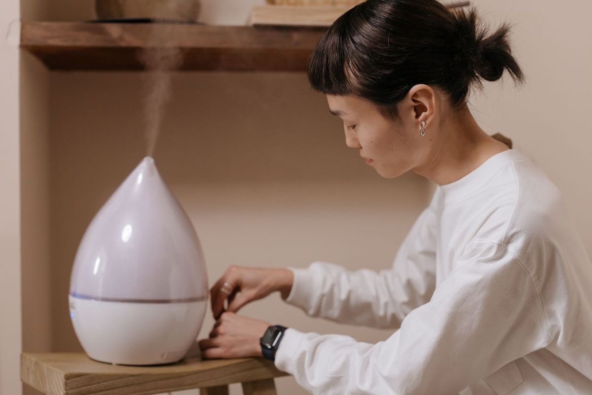 Woman in a white sweater sitting beside a wooden table with a humidifier running (representative photo, not the exact product)