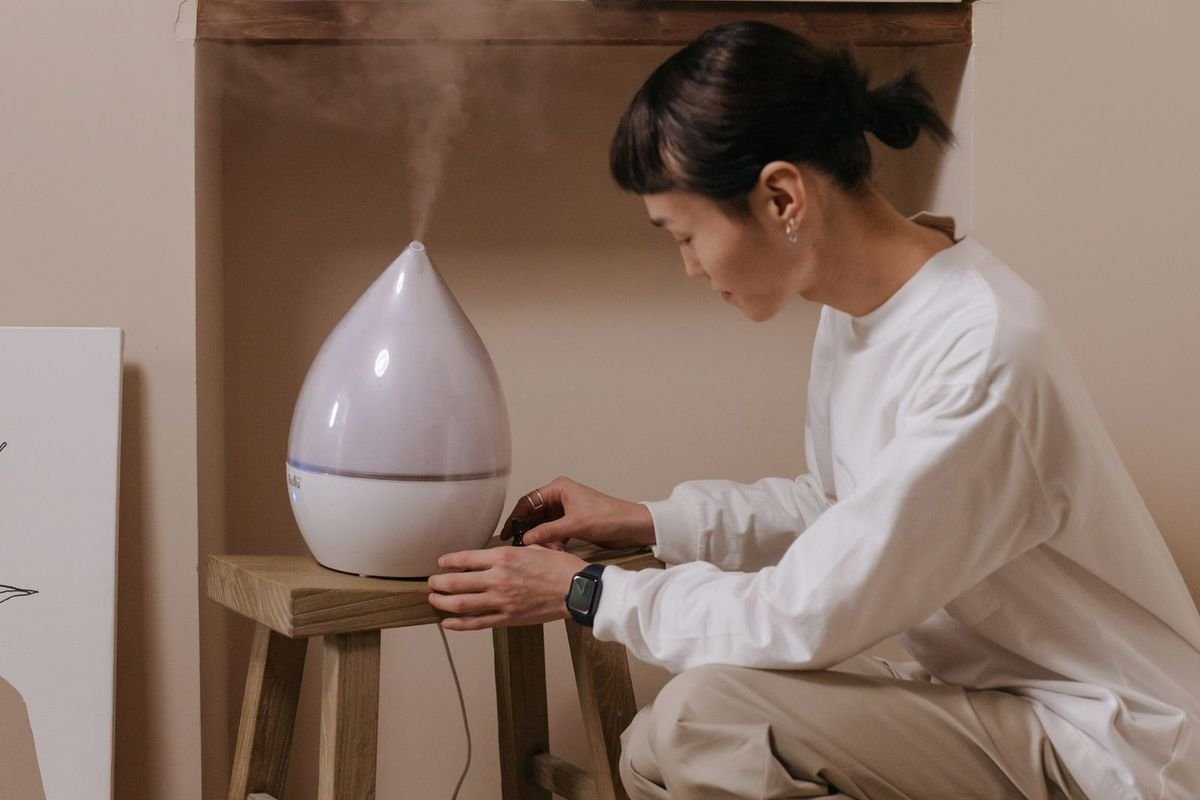 Woman kneeling beside a white humidifier on a small wooden stool in a cozy room (representative photo, not the exact product)