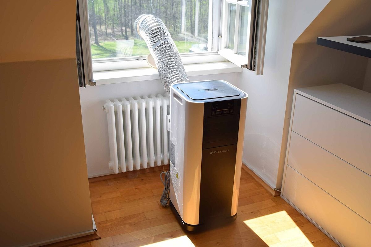Black and white portable air conditioner with its exhaust hose to a window (representative photo, not the exact product)