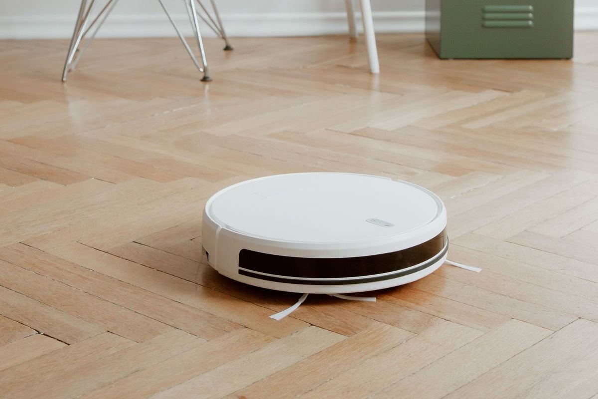 White robot vacuum and mop on a light herringbone wood floor beside a desk (representative photo, not the exact product)