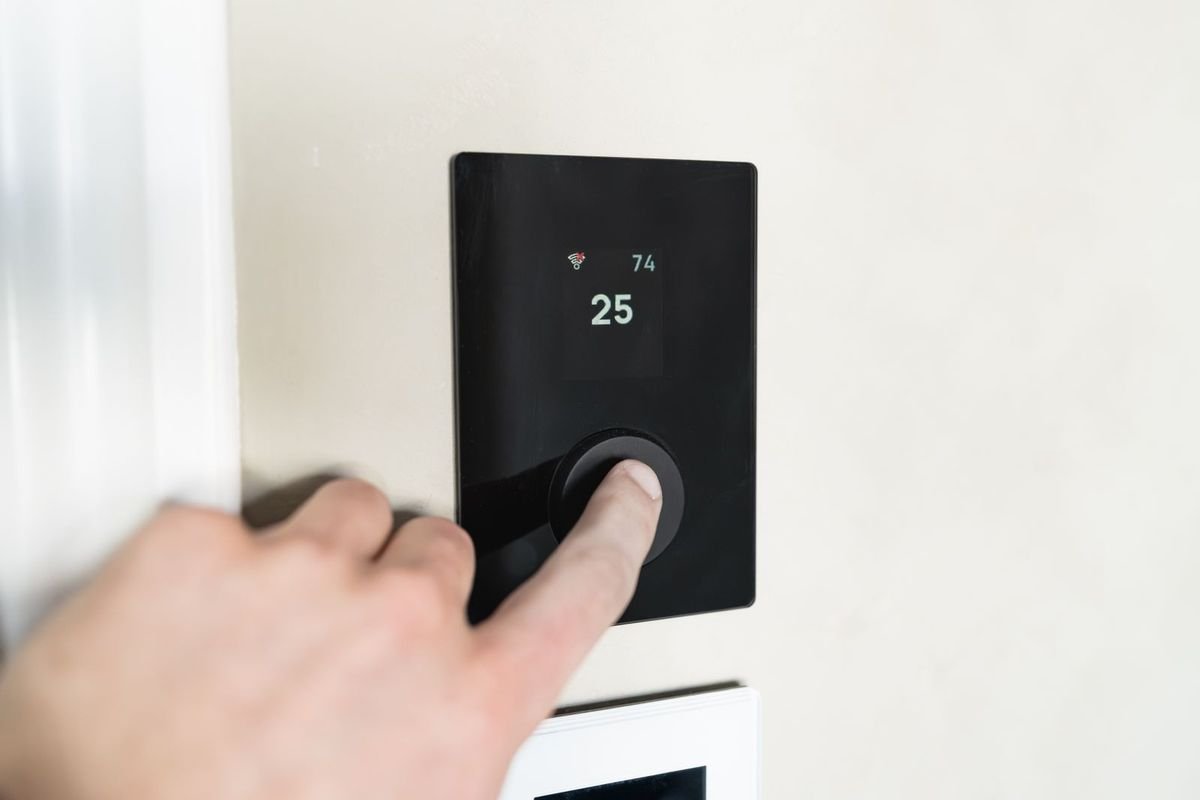 Hand adjusting a sleek digital temperature controller on a wall (representative photo, not the exact product)
