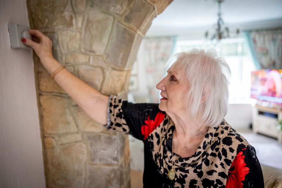 Older woman adjusting a temperature controller on a wall at home (representative photo, not the exact product)