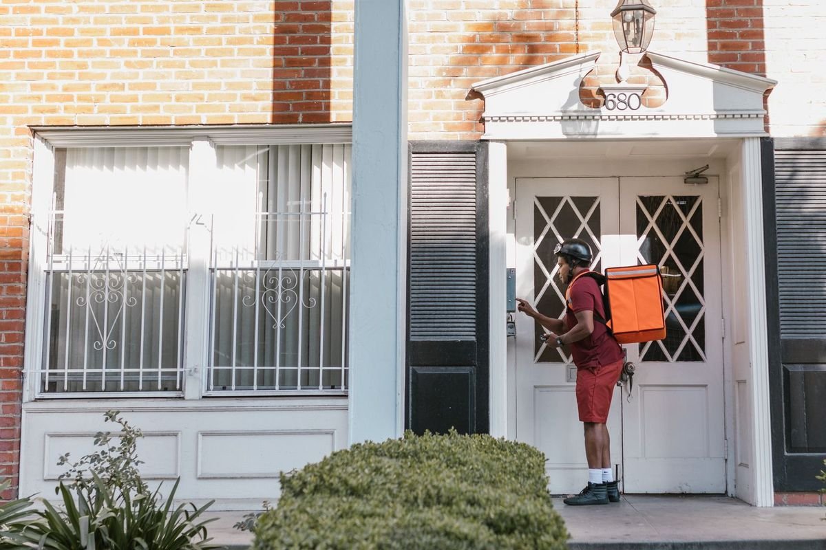 Delivery person with a package pressing a doorbell at a house entrance (representative photo, not the exact product)