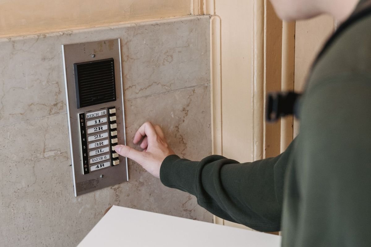 Courier holding a package pressing an intercom doorbell button (representative photo, not the exact product)