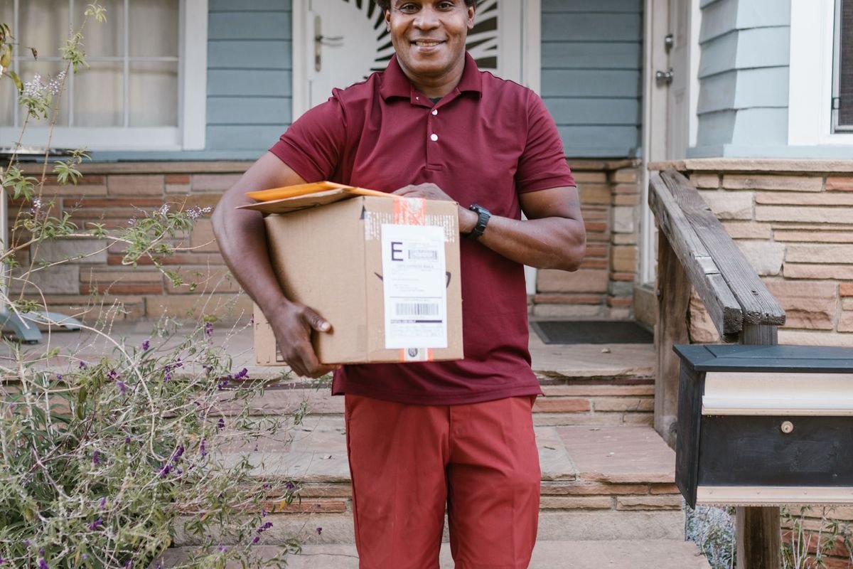 Courier in a red shirt carrying a box up to a front porch (representative photo, not the exact product)